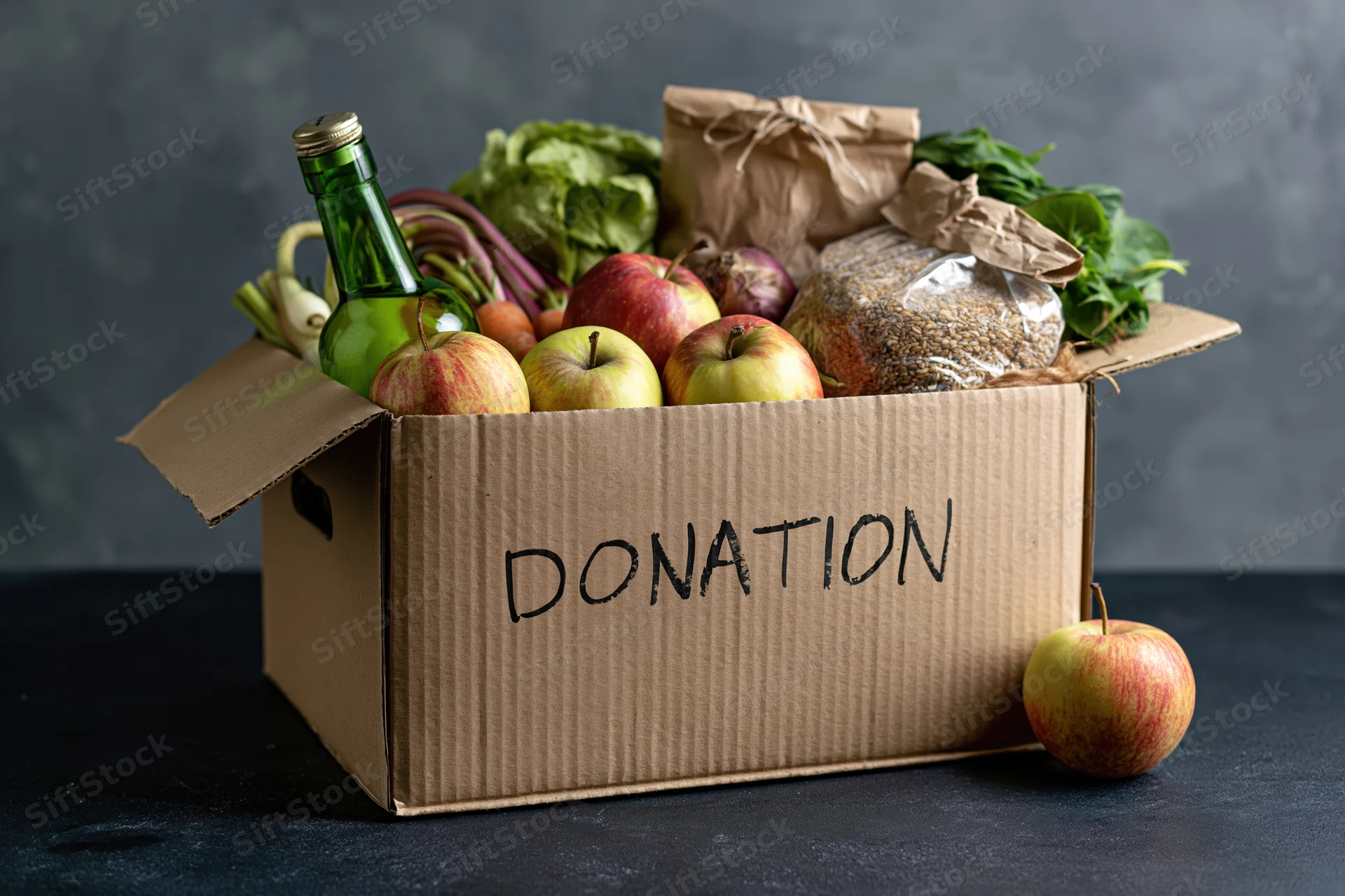 Cardboard box labeled donation filled with fresh produce and groceries on dark surface