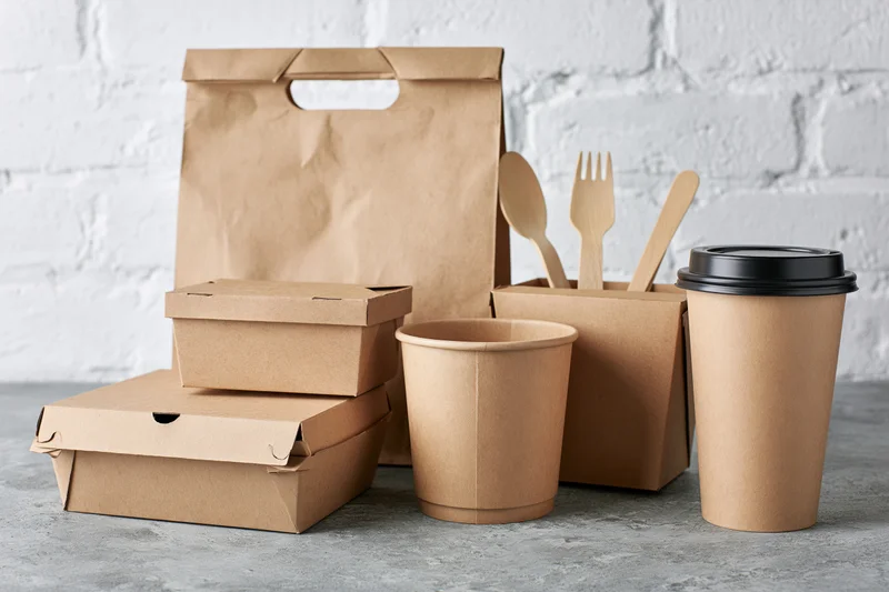 Kraft paper food packaging arranged on a grey concrete surface against a white brick wall
