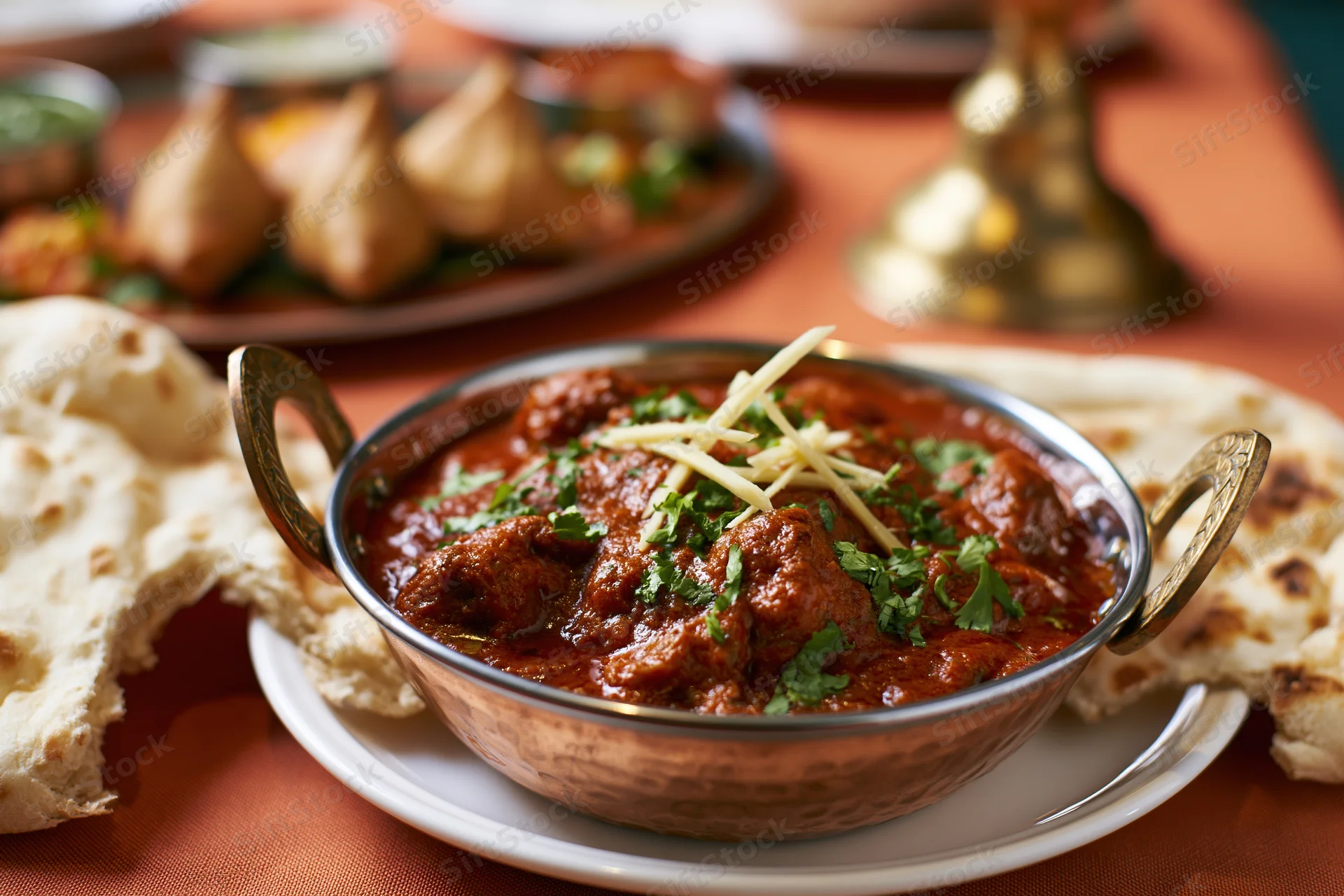 Copper karahi bowl filled with red curry garnished with cilantro and cheese, served with naan bread on a table