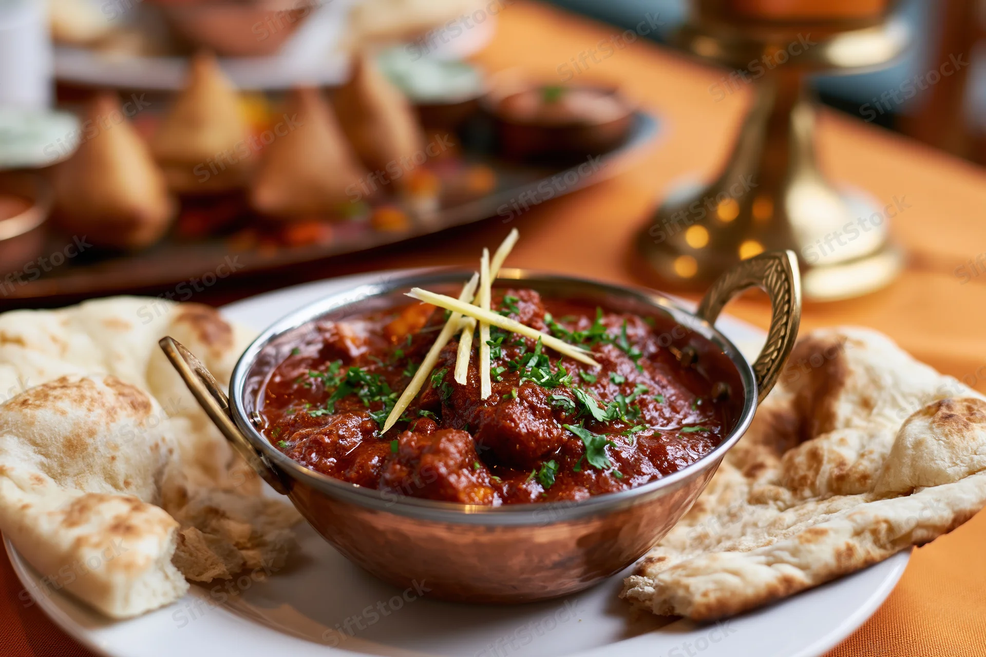 Copper karahi bowl filled with red curry garnished with ginger and cilantro, served with naan bread on a white plate at a dining table