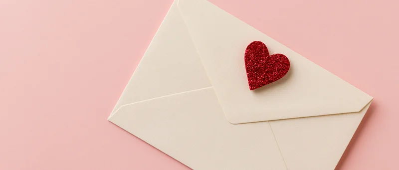 Cream envelope with red glitter heart on pink background