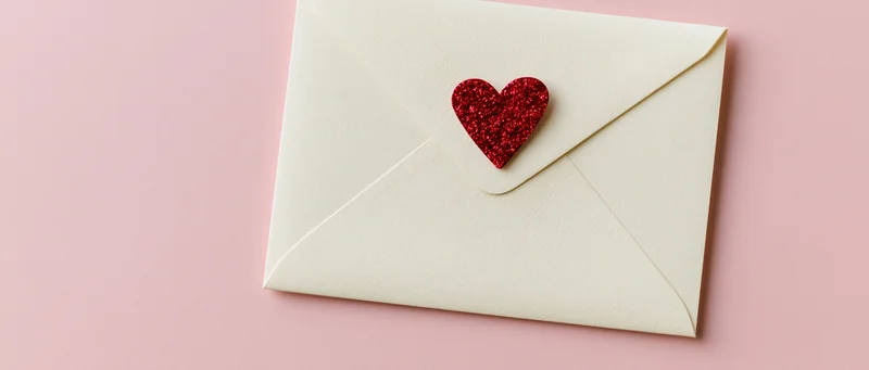 Cream envelope with red glitter heart on pink background