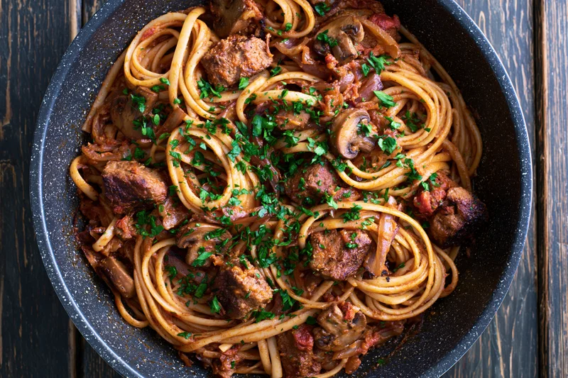 Linguine with meat and mushrooms in a dark speckled frying pan on a wooden table
