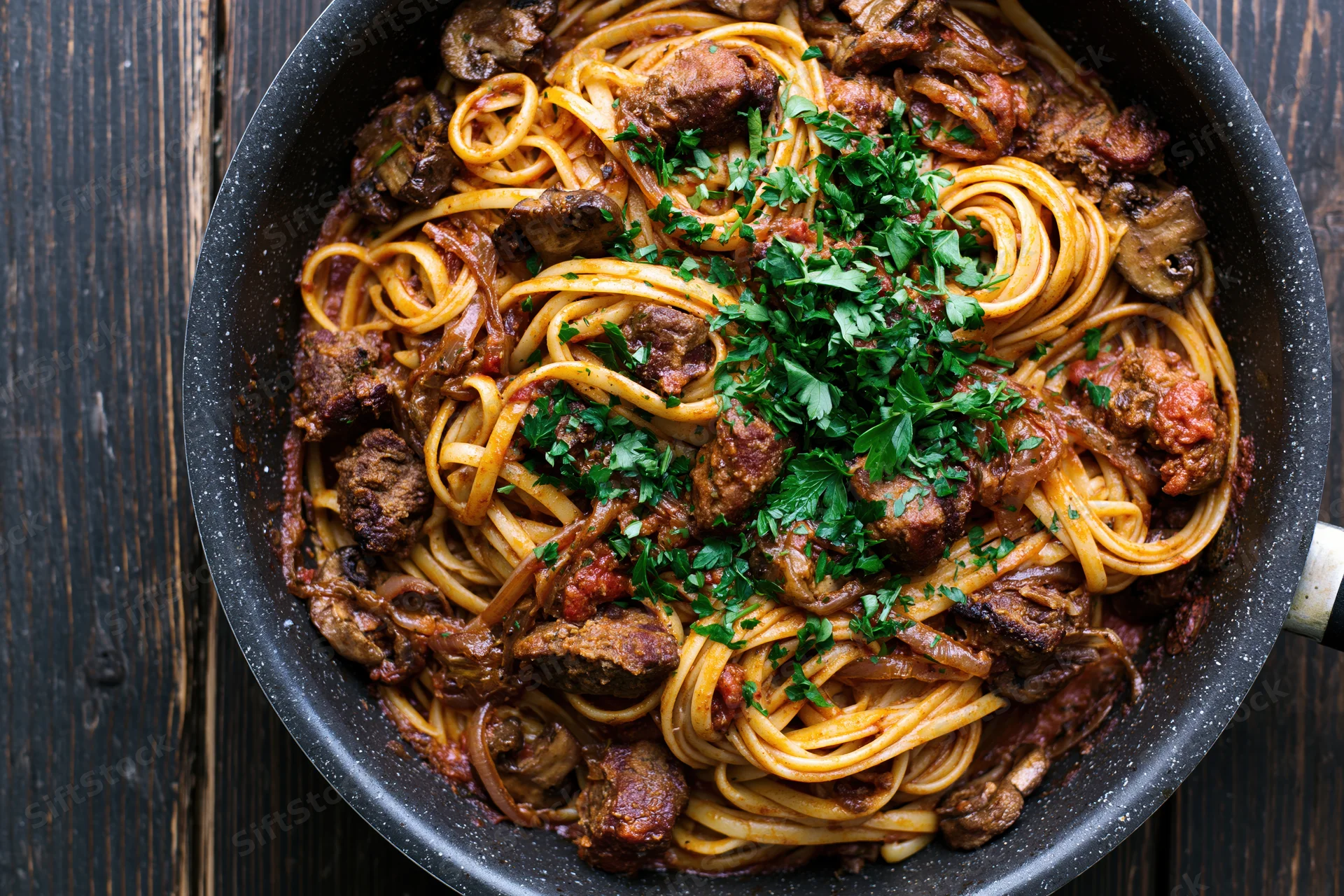 Linguine with meat and mushrooms in a speckled nonstick pan on a dark wooden surface