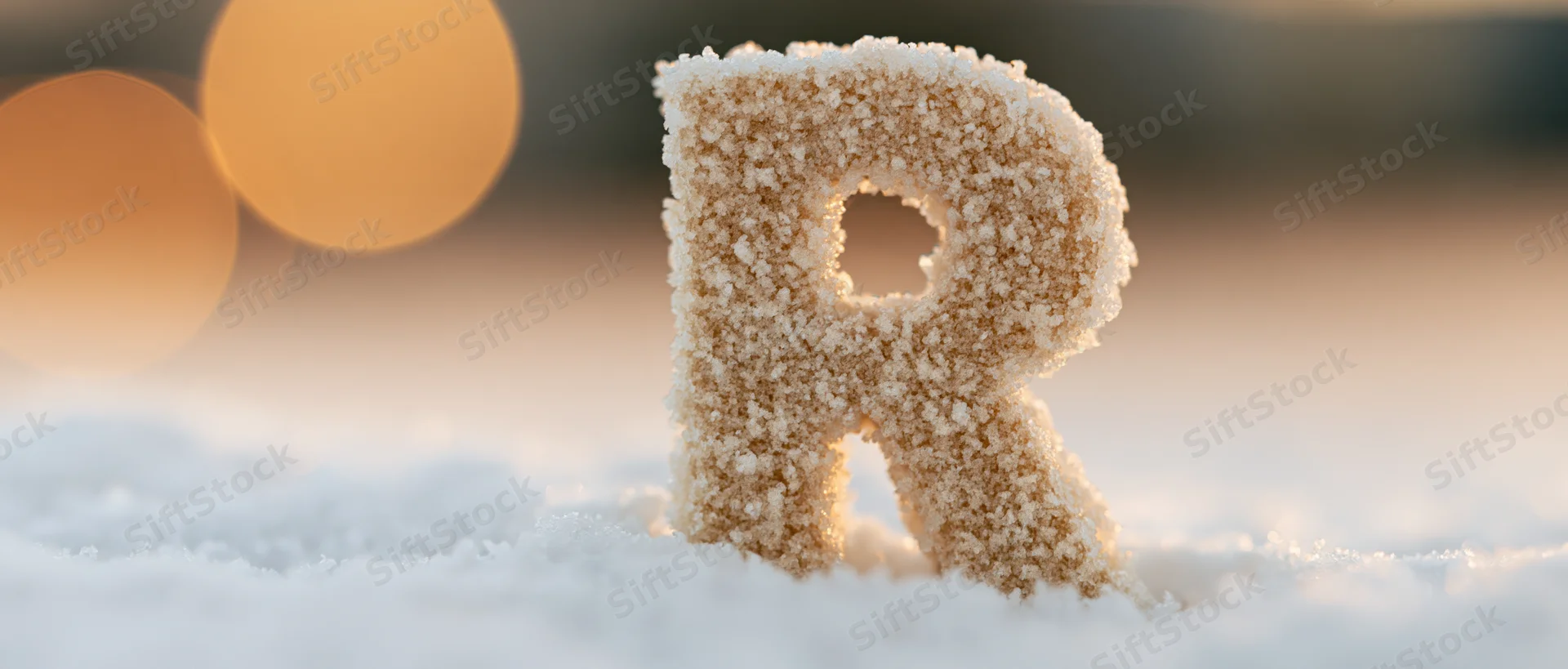 Frost-covered letter r standing in snow with warm bokeh lights in background
