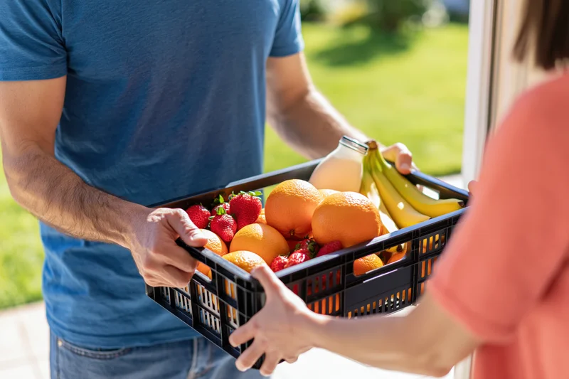 Delivery man handing a basket of fresh fruit and milk to a woman at a door