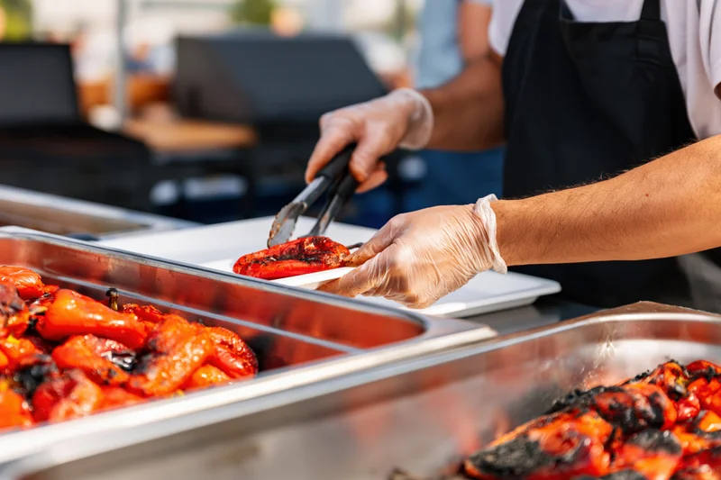 Food service worker serving grilled peppers from a buffet tray outdoors