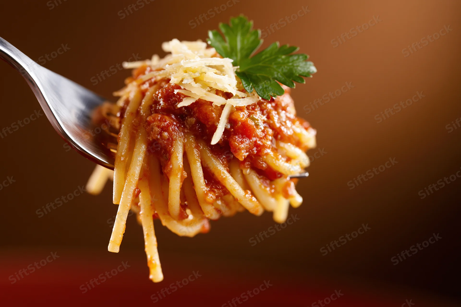 Fork holding spaghetti with tomato sauce, cheese and parsley against warm background