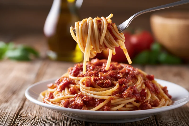 Fork twirling spaghetti with tomato sauce and pancetta lifted from a plate on a wooden table