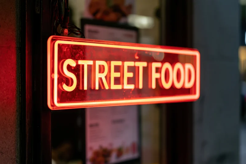 Glowing red neon sign reading street food mounted on a storefront exterior at night