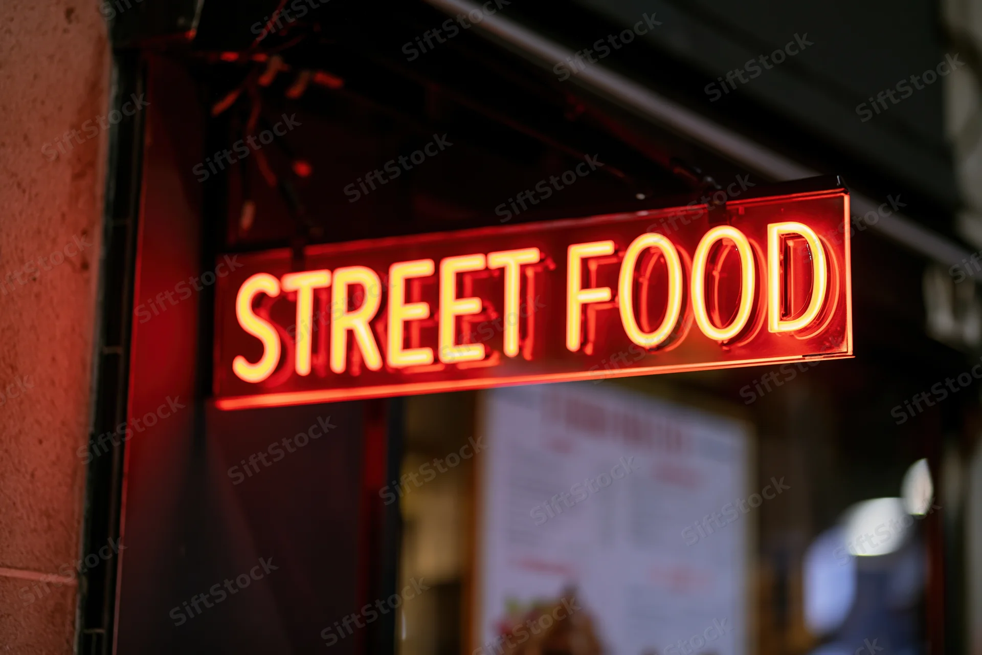 Glowing red neon sign reading street food mounted on a storefront exterior at night