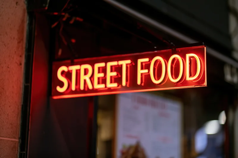 Glowing red neon sign reading street food mounted on a storefront exterior at night