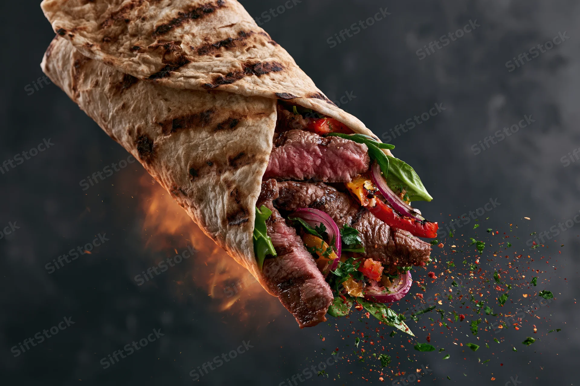 Grilled beef wrap mid-air with sliced steak and fresh greens bursting from the tortilla against a dark background