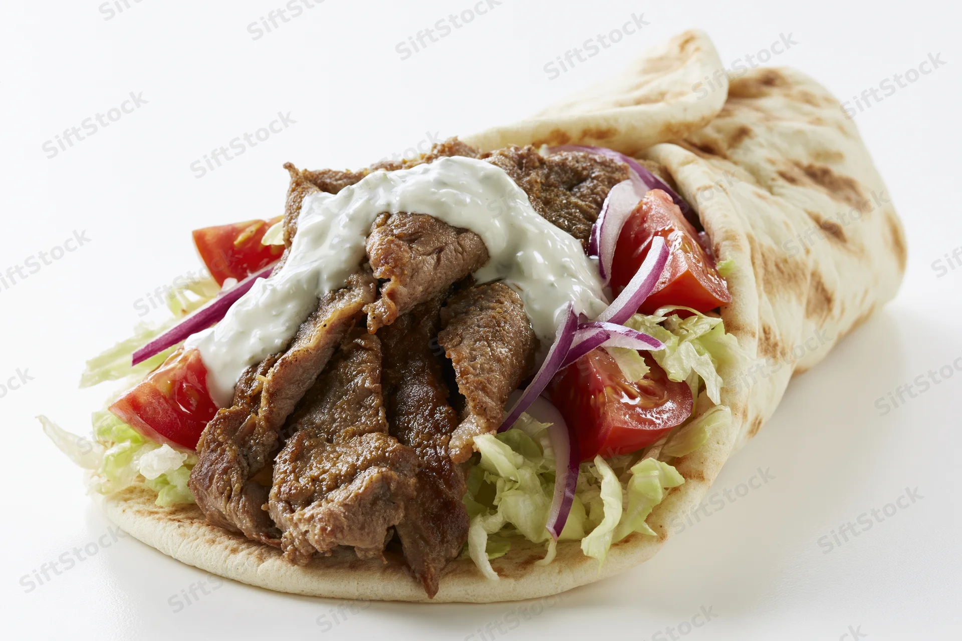 Gyro wrap filled with seasoned meat, shredded lettuce, tomato, red onion and creamy sauce on white background
