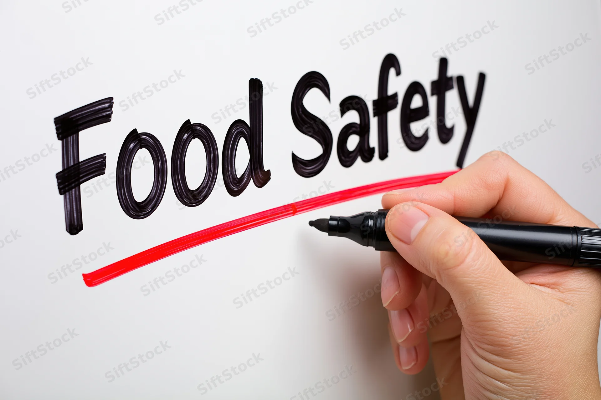 Hand writing food safety with black marker and red underline on white surface