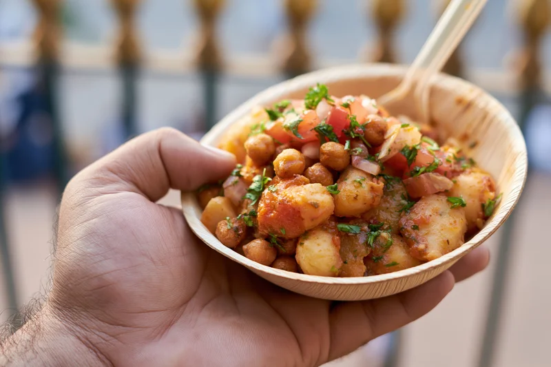 Hand holding a paper leaf bowl of indian street food with chickpeas and potatoes outdoors