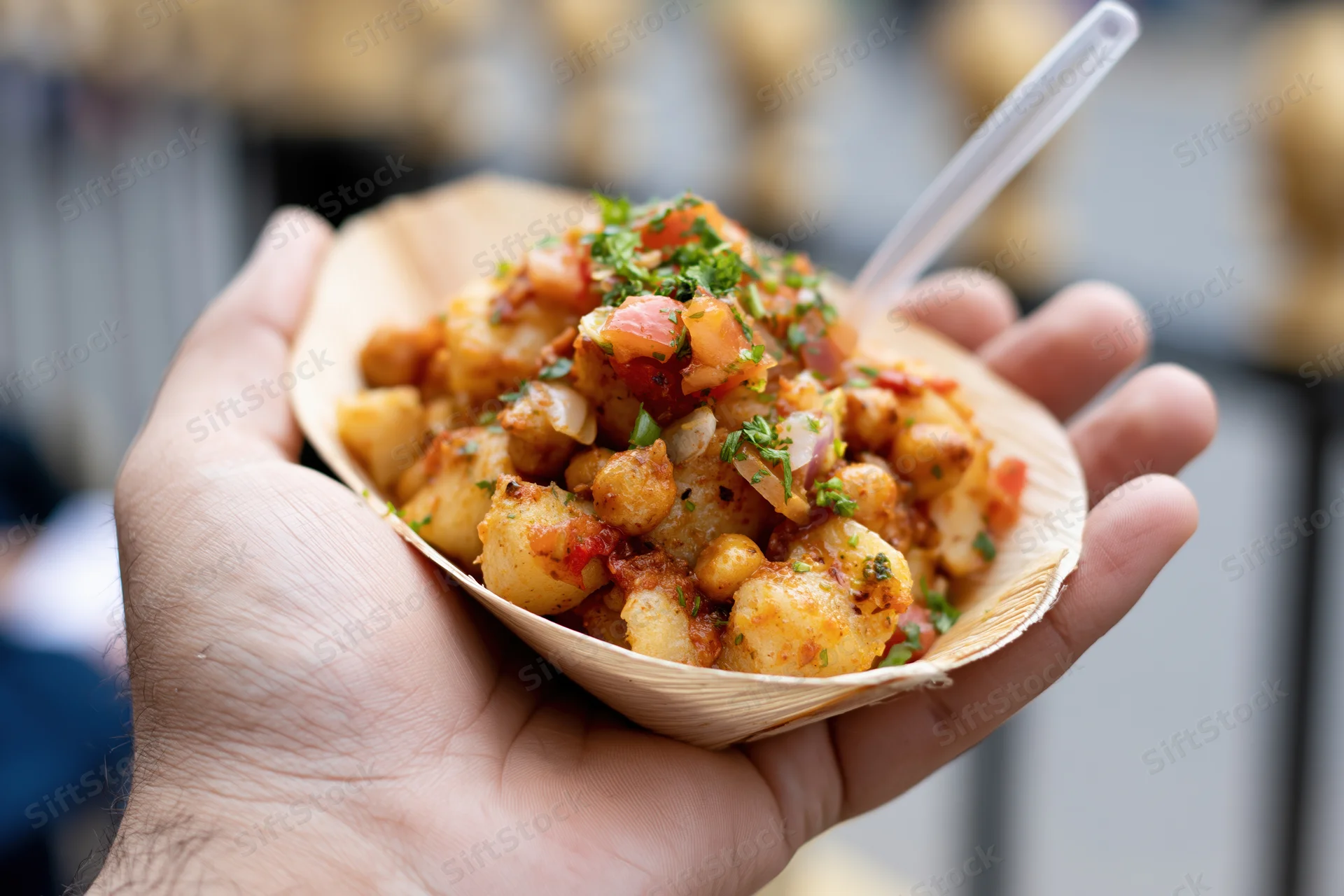 Hand holding a paper leaf bowl filled with spiced chickpea street food snack outdoors