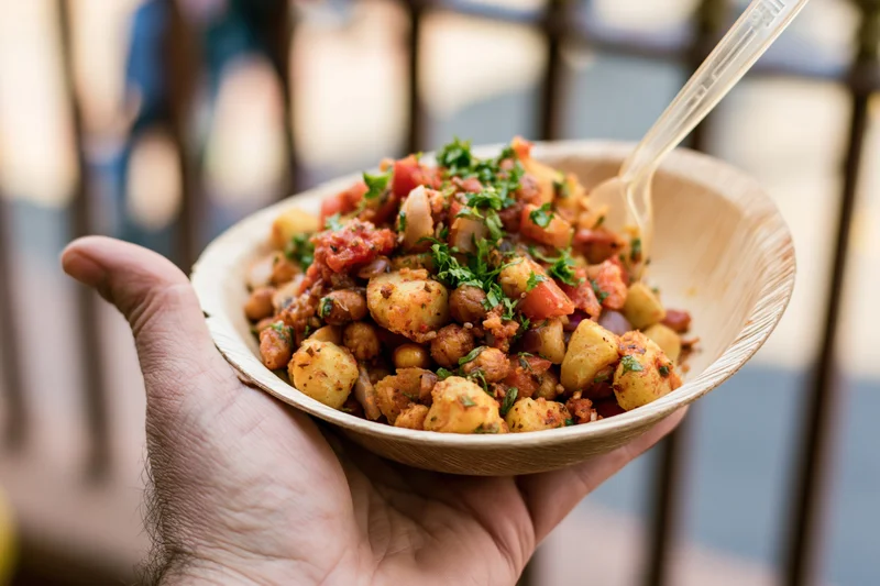 Hand holding a paper leaf bowl filled with indian street food snack outdoors