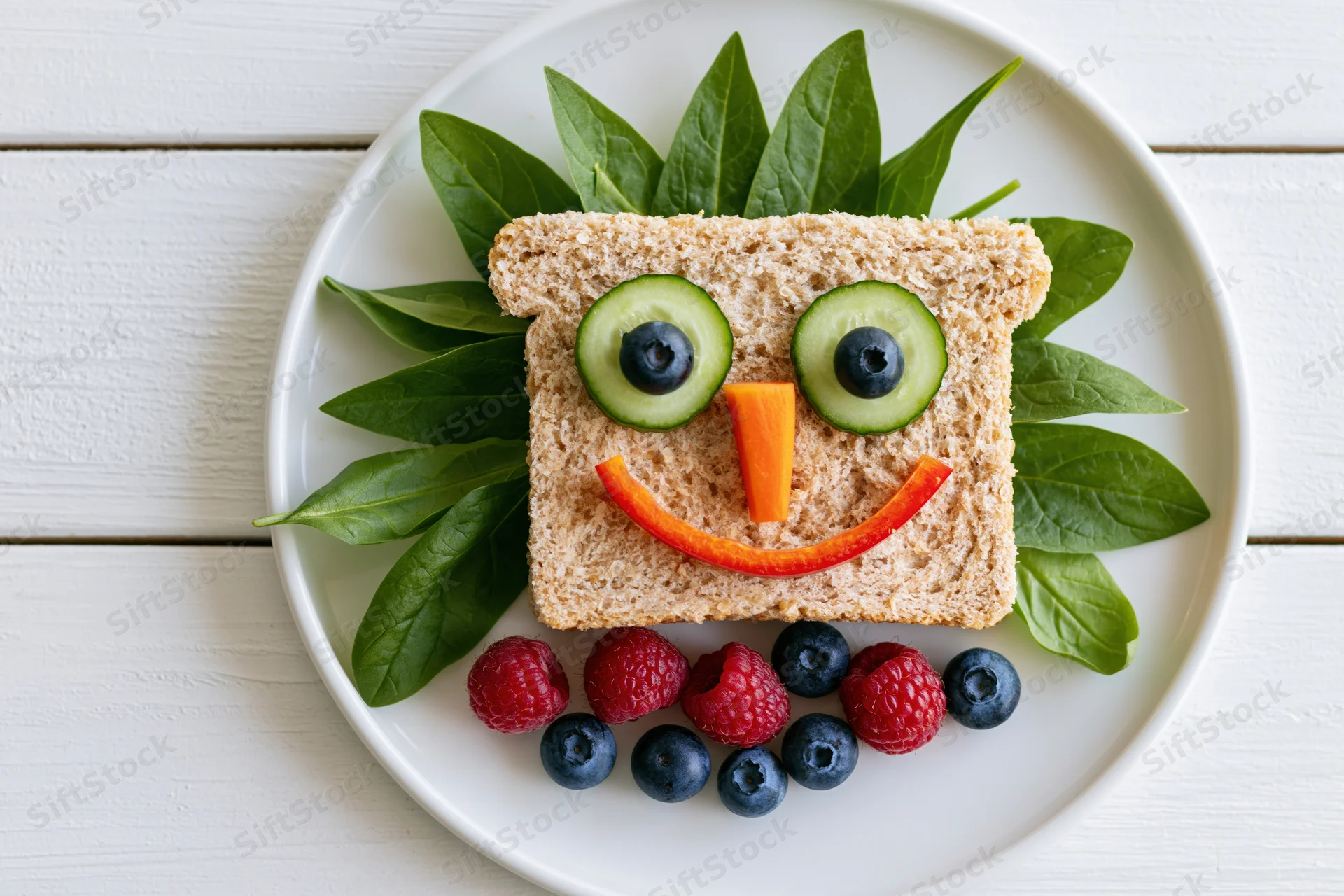 Kids sandwich decorated as a smiley face on a white plate with vegetables and berries