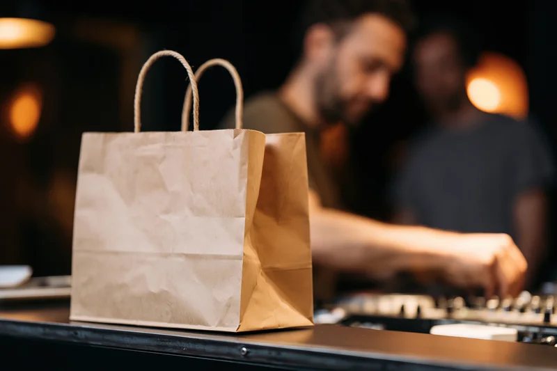 Kraft paper takeout bag with rope handles on a dj console in a dimly lit club setting