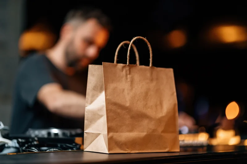 Kraft paper takeout bag with rope handles on a table in front of a dj at a club event