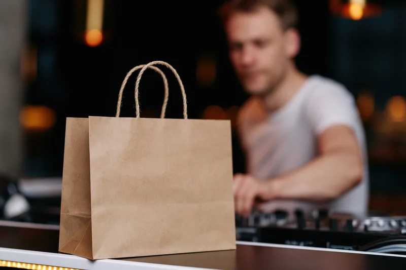 Kraft paper takeout bag with rope handles on a dj table in a dimly lit nightclub