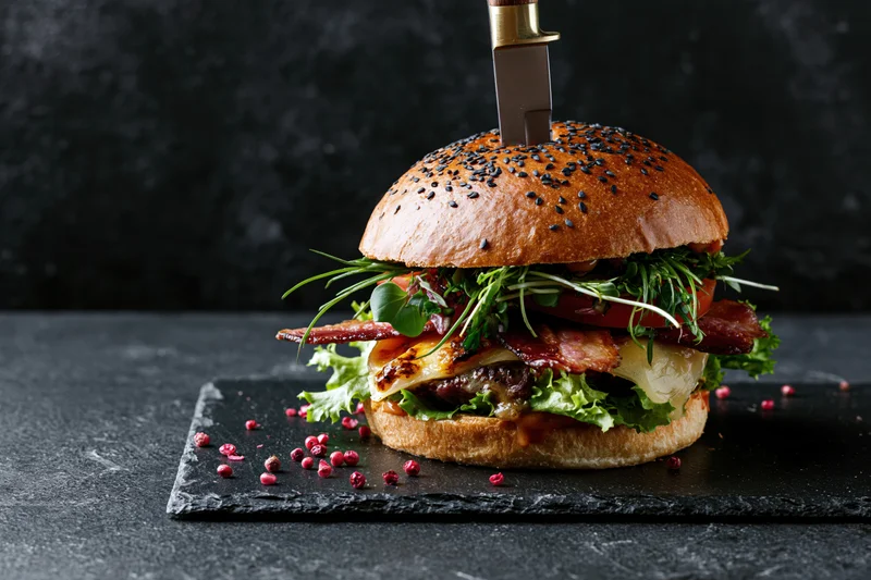 Large gourmet burger with steak knife stabbed vertically on slate plate
