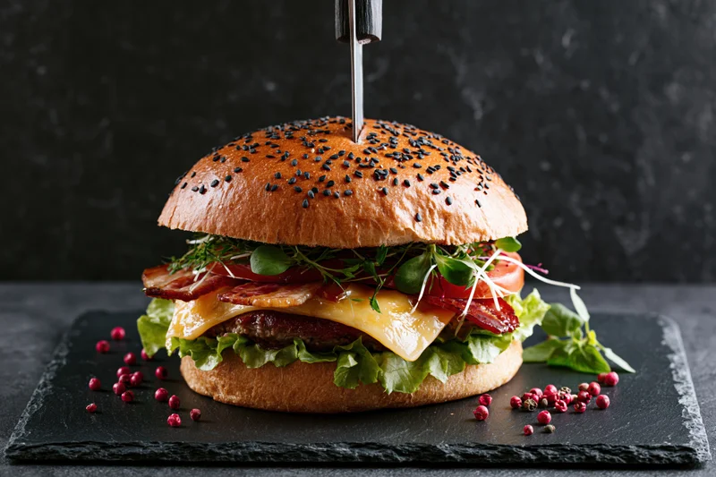Large gourmet burger with steak knife stabbed vertically on slate plate