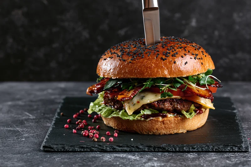Large gourmet burger with steak knife stabbed vertically on slate plate