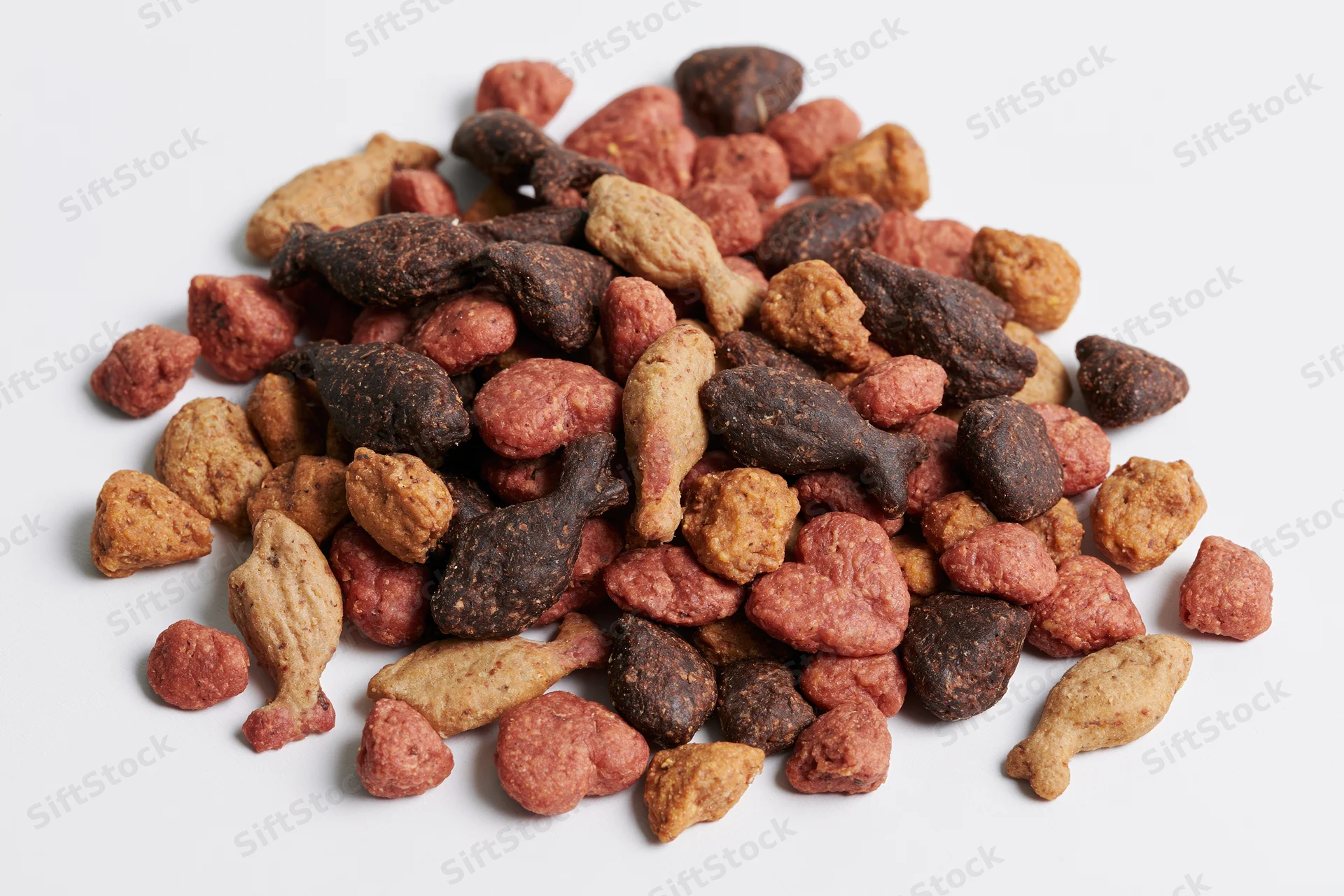 Pile of dry cat food kibble in mixed shapes and colors on white background