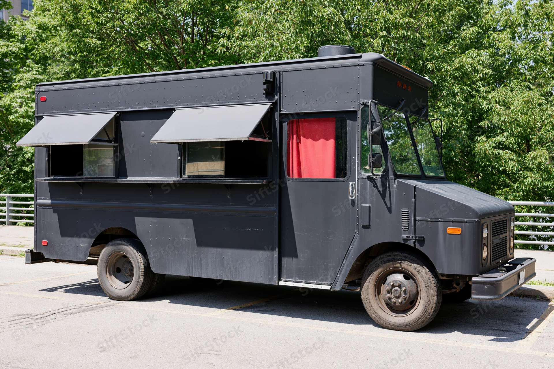 Matte black food truck parked on paved urban lot with awnings extended and red curtain visible through side window
