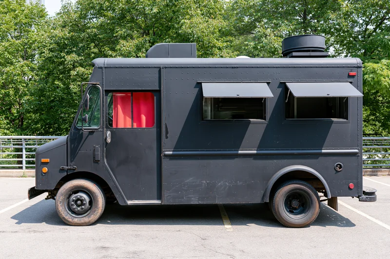 Matte black food truck parked in an urban lot with side windows and awnings