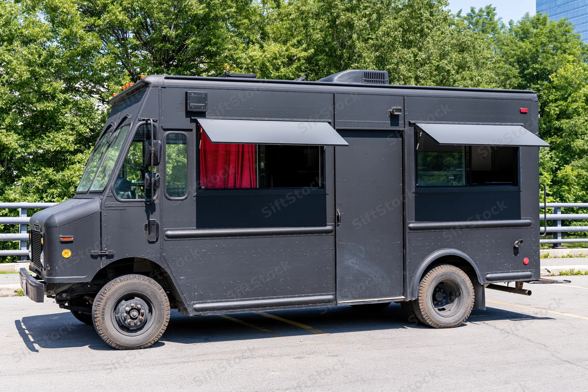 Matte black food truck parked on paved urban lot with awnings and red curtains visible through windows