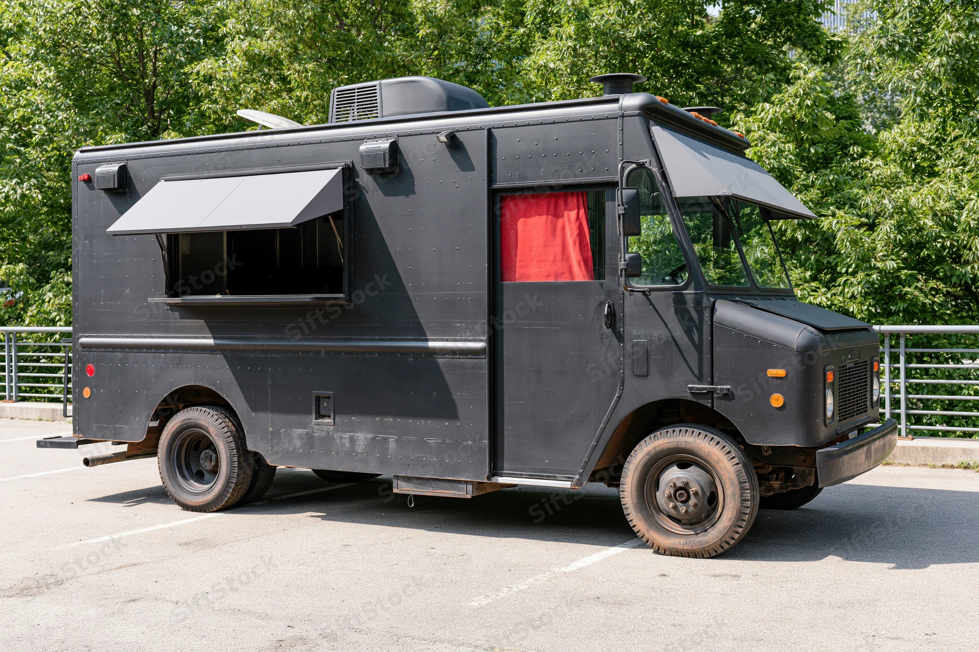 Matte black food truck parked on paved urban lot with awning extended and red curtain visible through window
