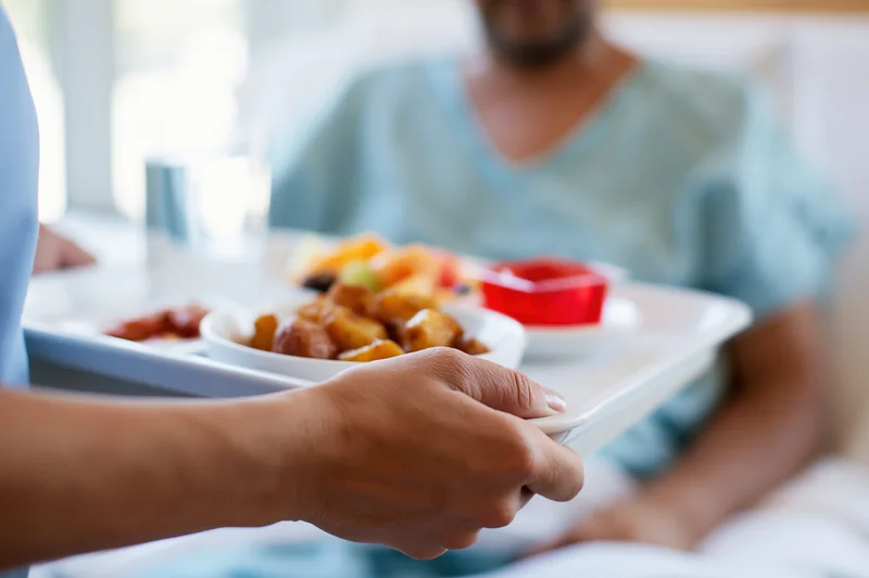 Nurse placing hospital meal tray in front of patient in bed