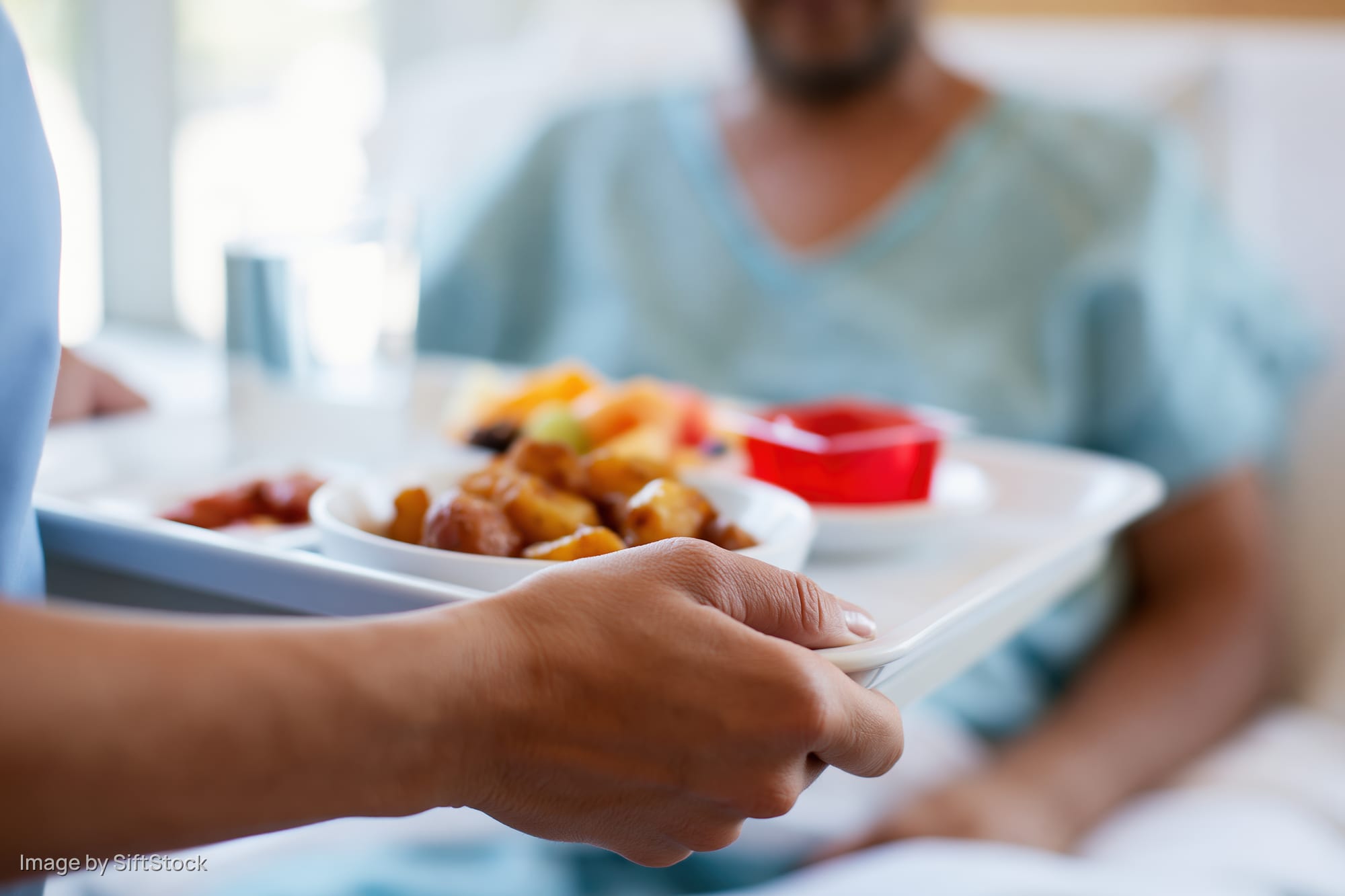 Nurse placing hospital meal tray in front of patient in bed