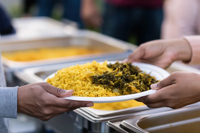 Hands passing a plate of yellow rice and green vegetables at a food donation event