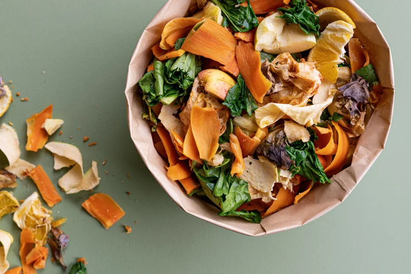 Paper bag filled with mixed vegetable scraps and food waste on green surface