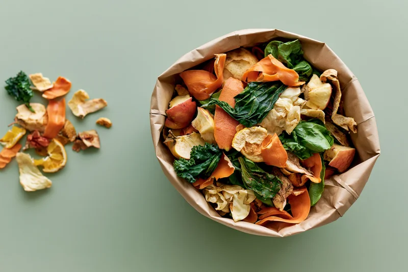 Paper bag filled with mixed vegetable scraps and food waste on a green surface