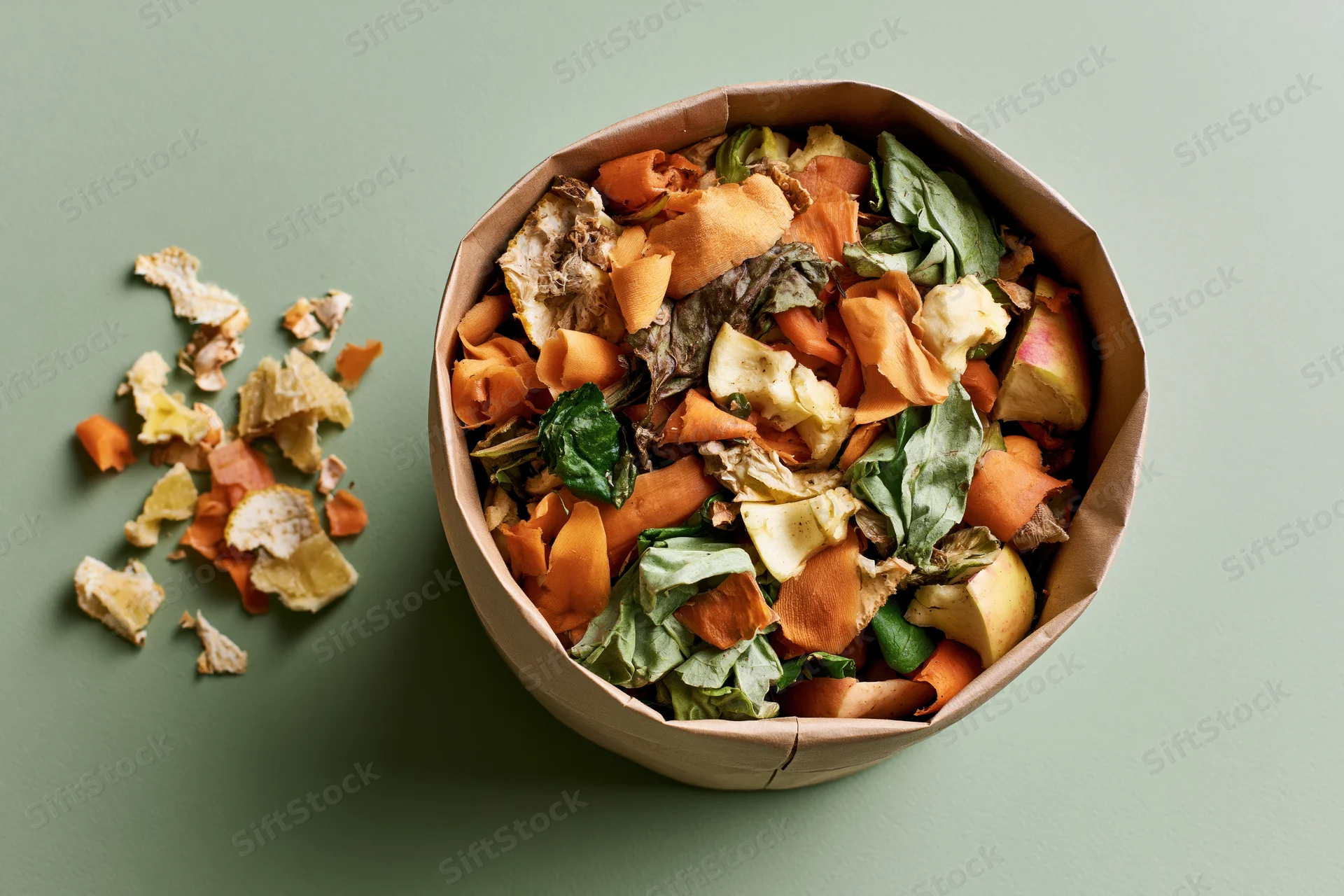 Paper bag filled with mixed vegetable scraps and food waste on a green surface