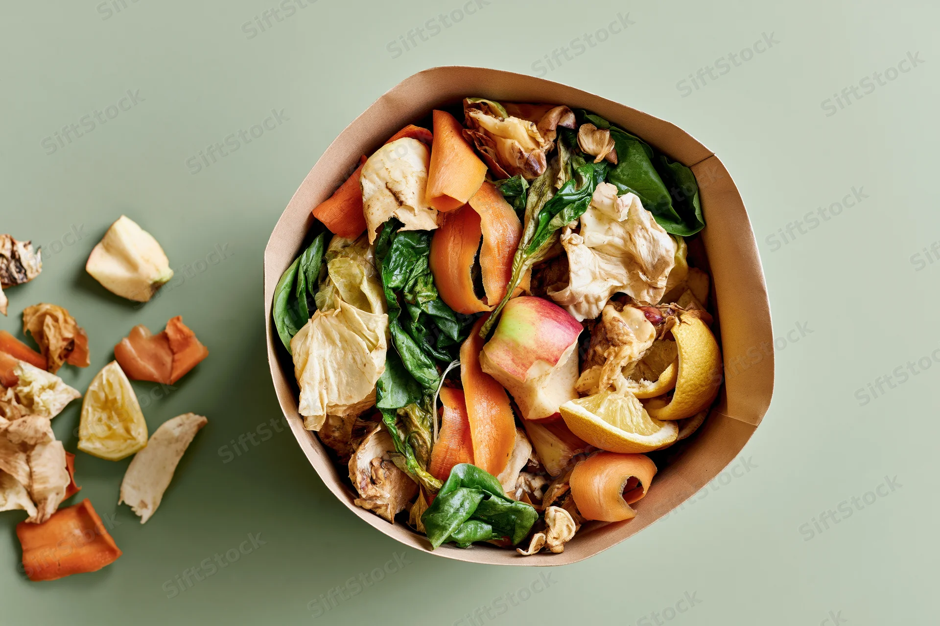 Paper bag filled with mixed vegetable and fruit scraps on a green surface