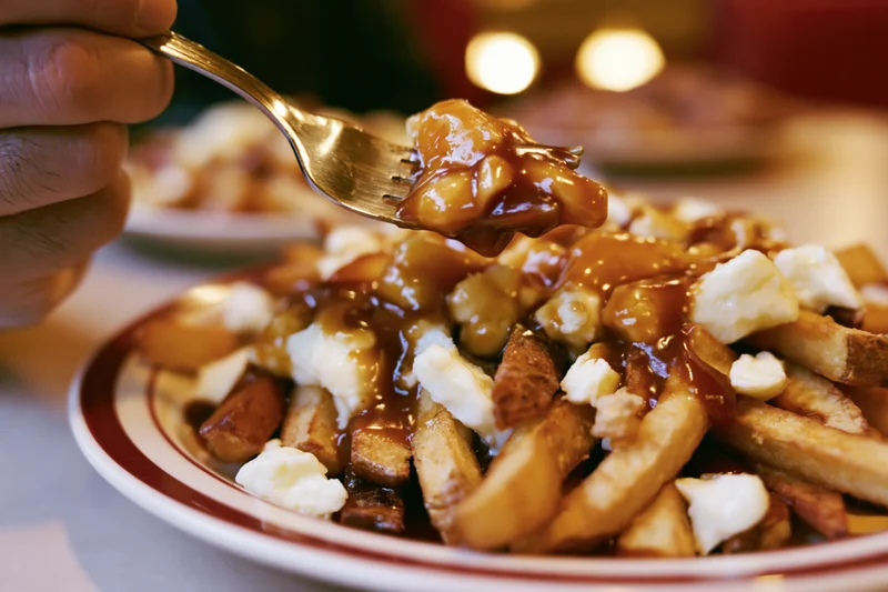 Hand lifting a forkful of poutine from a diner plate pile