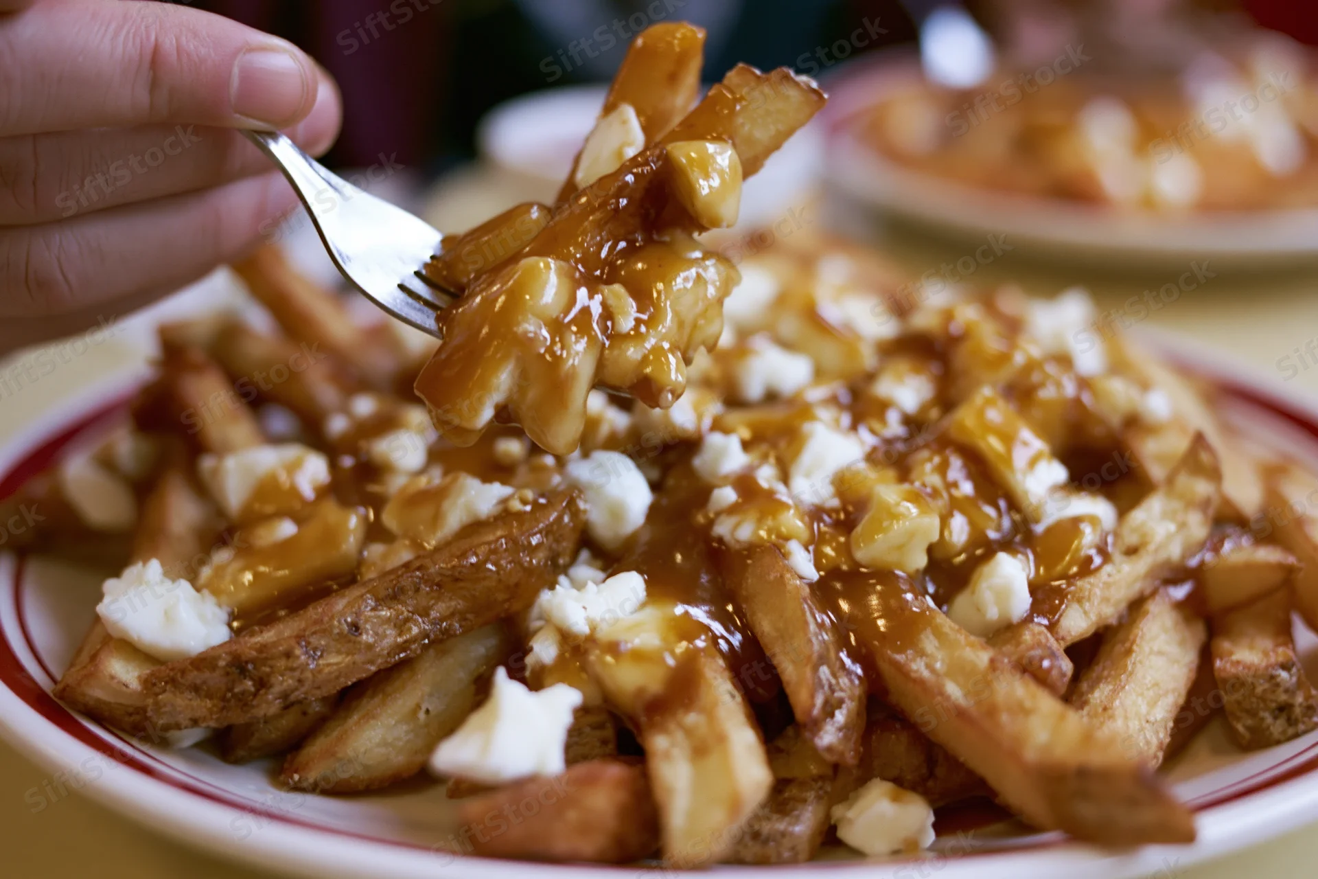 Hand lifting forkful of poutine from diner plate pile