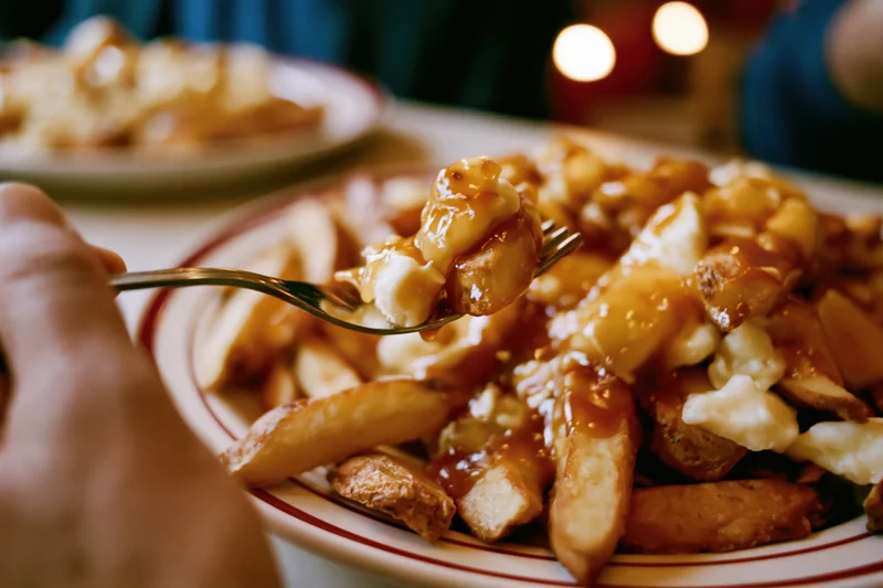 Hand lifting forkful of poutine from diner plate pile