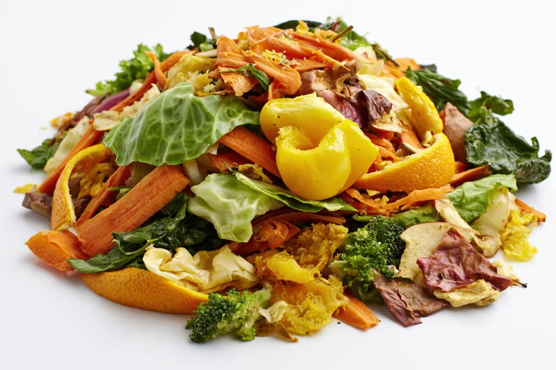 Pile of mixed vegetable and fruit kitchen scraps heaped on white background