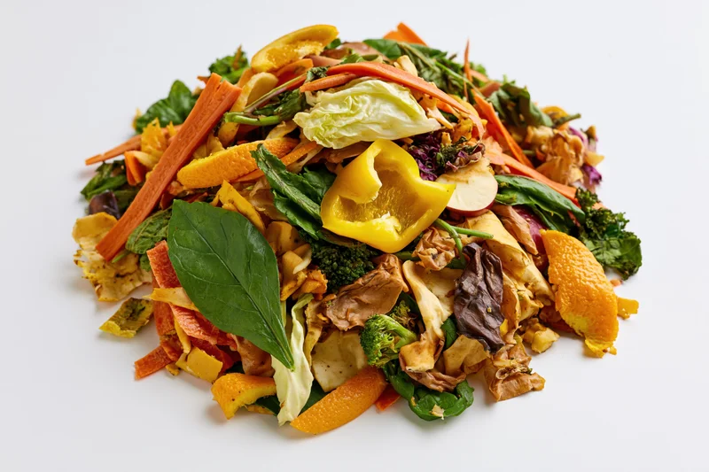 Pile of mixed vegetable and fruit kitchen scraps heaped on white surface
