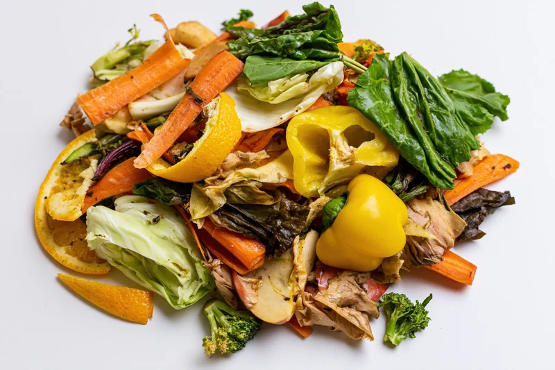 Pile of mixed vegetable and fruit kitchen scraps heaped on white surface