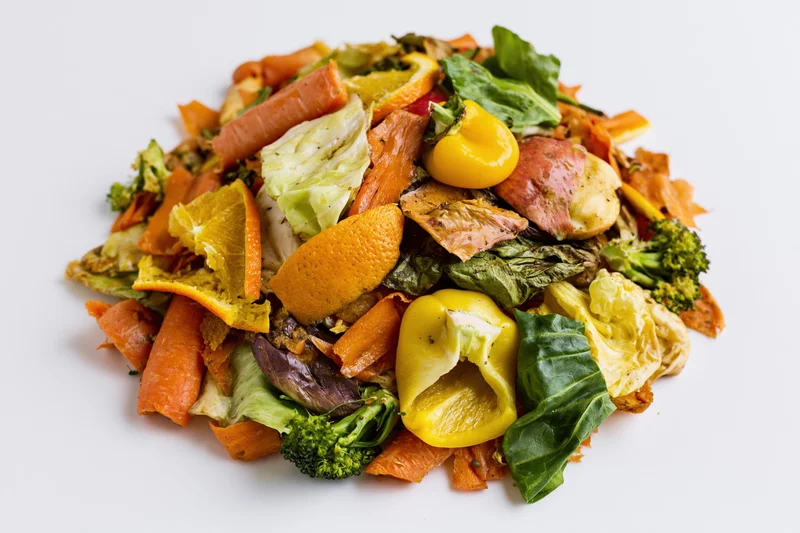 Pile of mixed vegetable and fruit kitchen scraps heaped on white surface