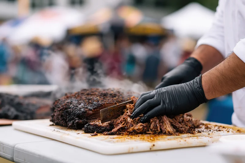 Pitmaster shredding smoked pork on a cutting board at an outdoor food festival