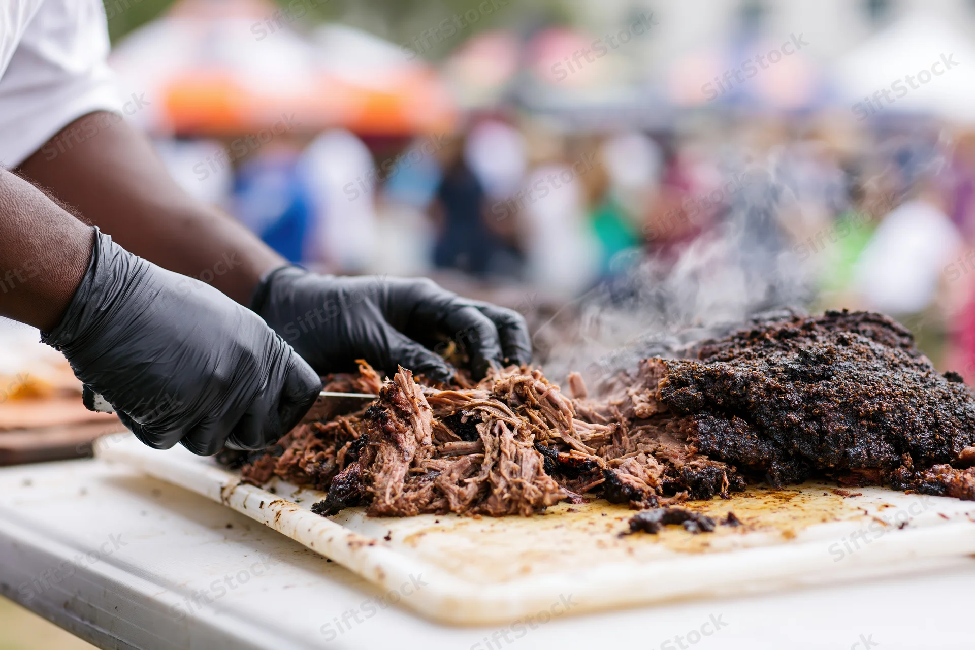 Pitmaster slicing smoked brisket on a white cutting board at an outdoor food festival